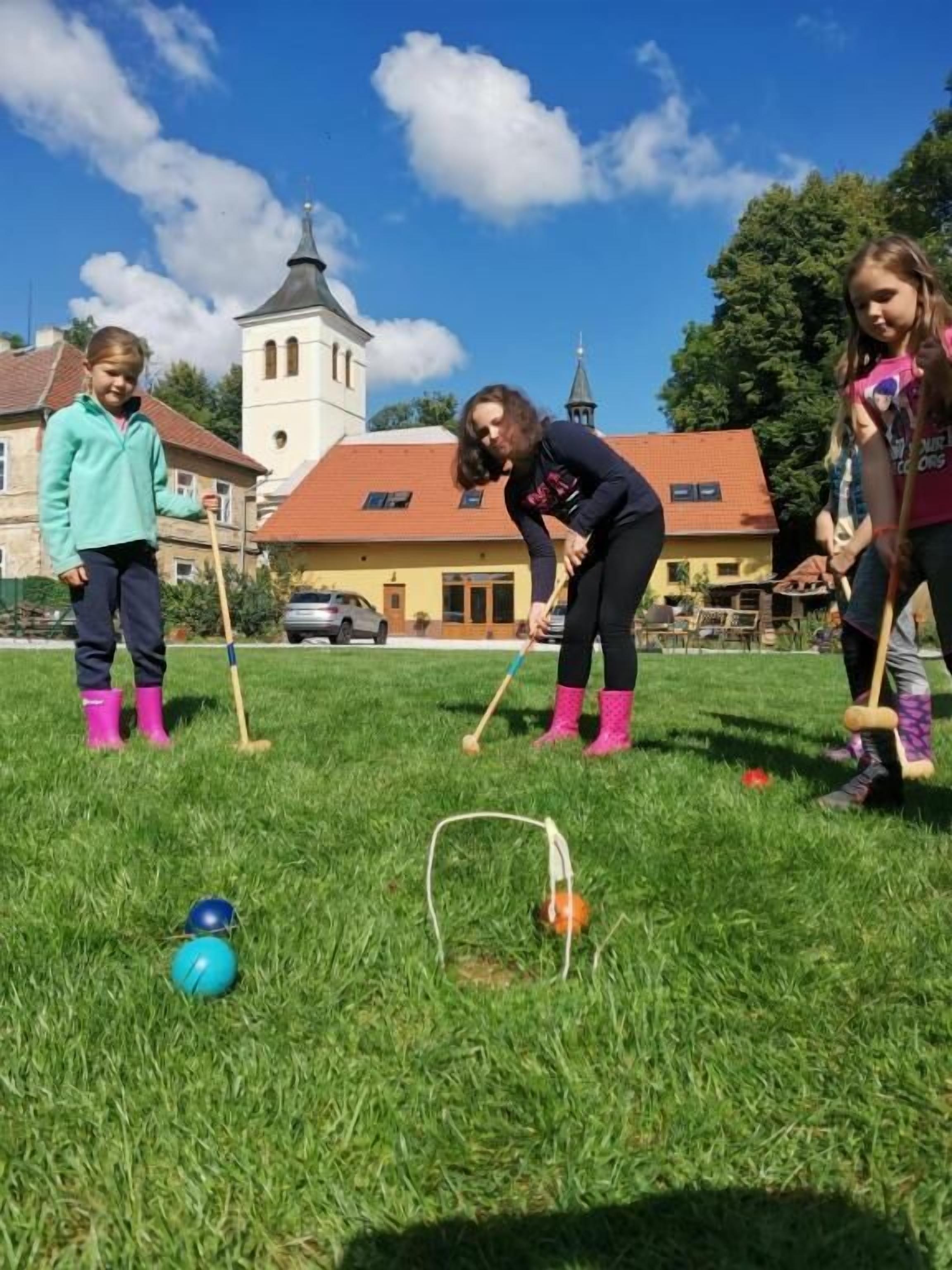 A group of people playing croquet on a grassy field with a church in the background.