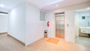 Ein moderner Aufzug mit digitaler Anzeige, einem an der Wand montierten Feuerlöscher und einer kleinen Mülltonne.