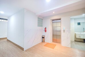 Un ascensor moderno con pantalla digital, un extintor en la pared y un pequeño bote de basura.
