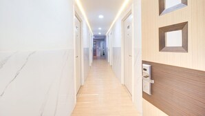 Ein Hotelkorridor mit Marmorboden, Holztüren und einer modernen Leuchte.