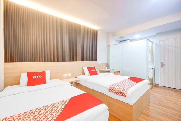 Habitación de hotel con dos camas, cabecero de madera, mesita de noche, espejo, armario y baño con ducha.