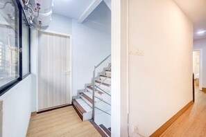 A hallway with a wooden floor, a white door, and a staircase with metal railings.