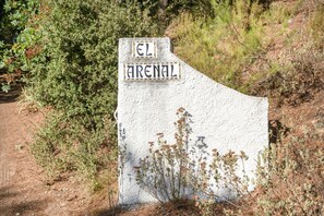 Un letrero de piedra blanca con la inscripción 'EL ARENAL' en letras negras, rodeado de vegetación natural.