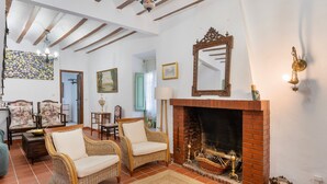 A cozy living room with a fireplace, wicker chairs, a dining area, and a hallway leading to another room.