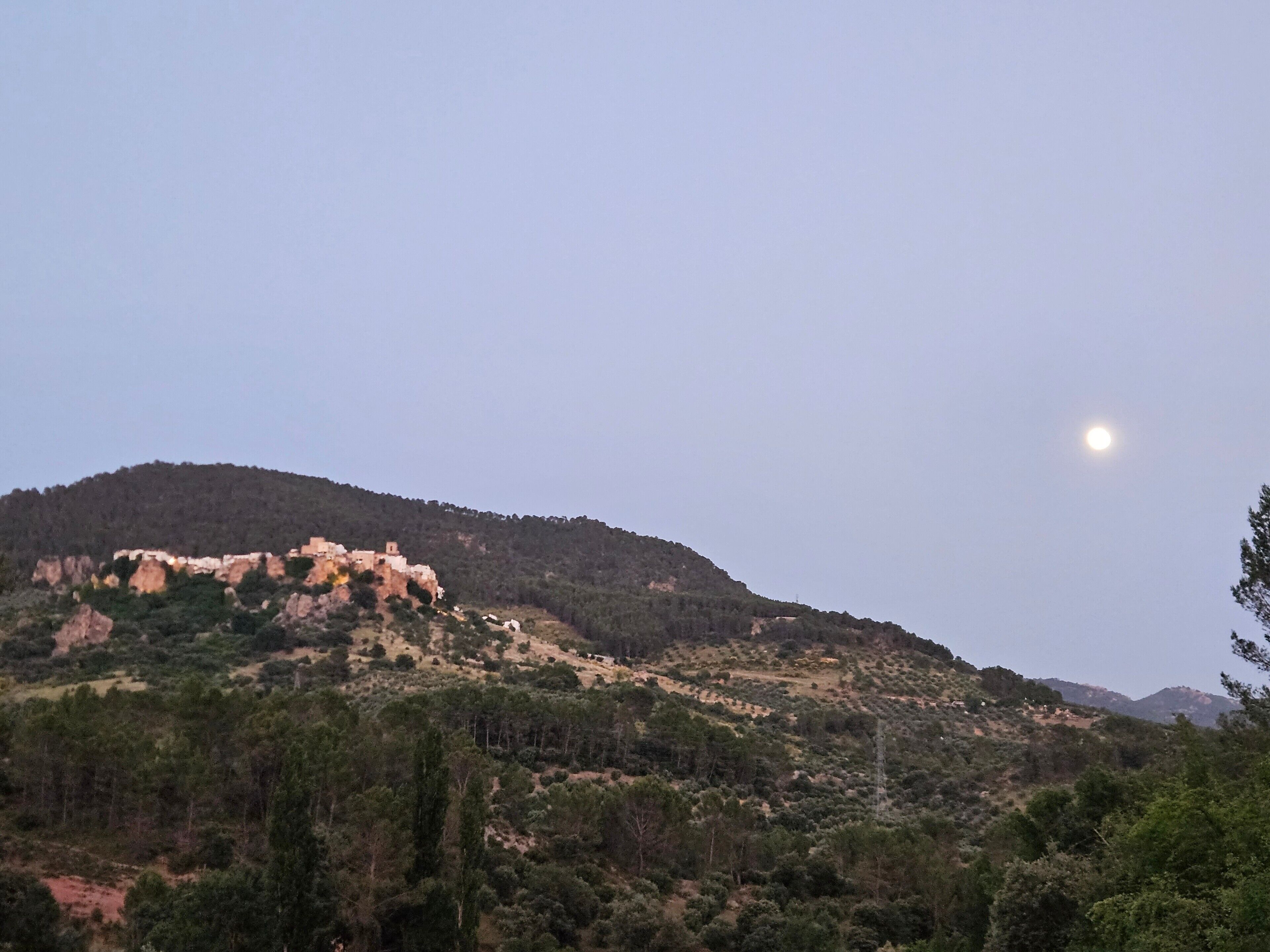 A mountainous landscape with a clear sky and a visible moon.
