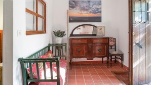 A room with a wooden cabinet, a bench with cushions, a potted plant, and a painting of a sunset on the wall.