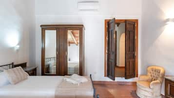 Ein Schlafzimmer mit einem Bett, einem Sessel, einem Kleiderschrank und einer Tür zu einem anderen Raum.