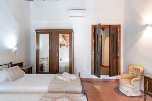 A bedroom with a bed, a chair, a wardrobe, and a door leading to another room.