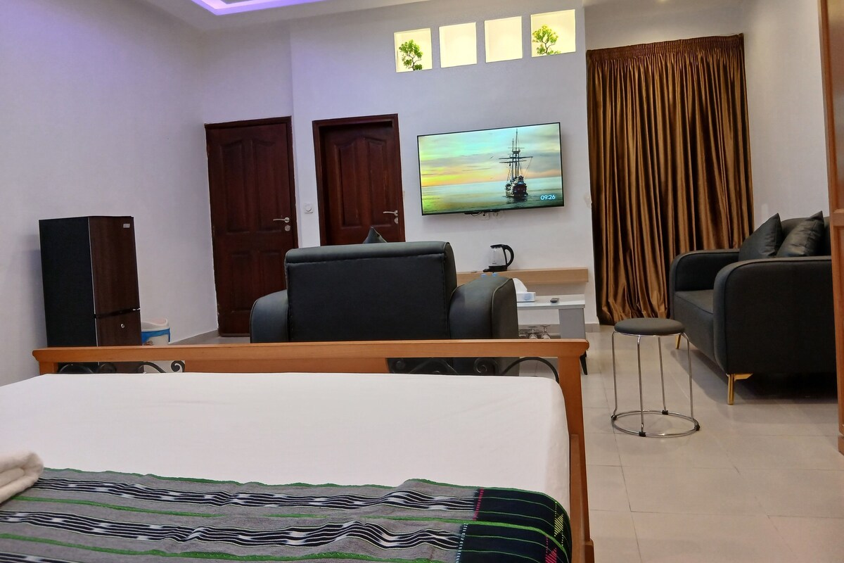 A hotel room with a bed, a desk, a chair, a sofa, a television, and a wardrobe.
