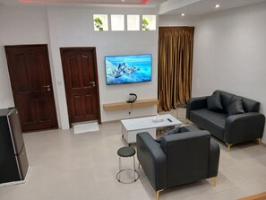 A modern living room with a flat-screen TV, a sofa, a coffee table, and a small stool. - Sheyllo Suites Abidjan (Abidjan)