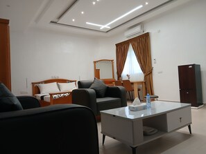A modern hotel room with a bed, two sofas, a coffee table, a desk, and a wardrobe. - Sheyllo Suites Abidjan (Abidjan)