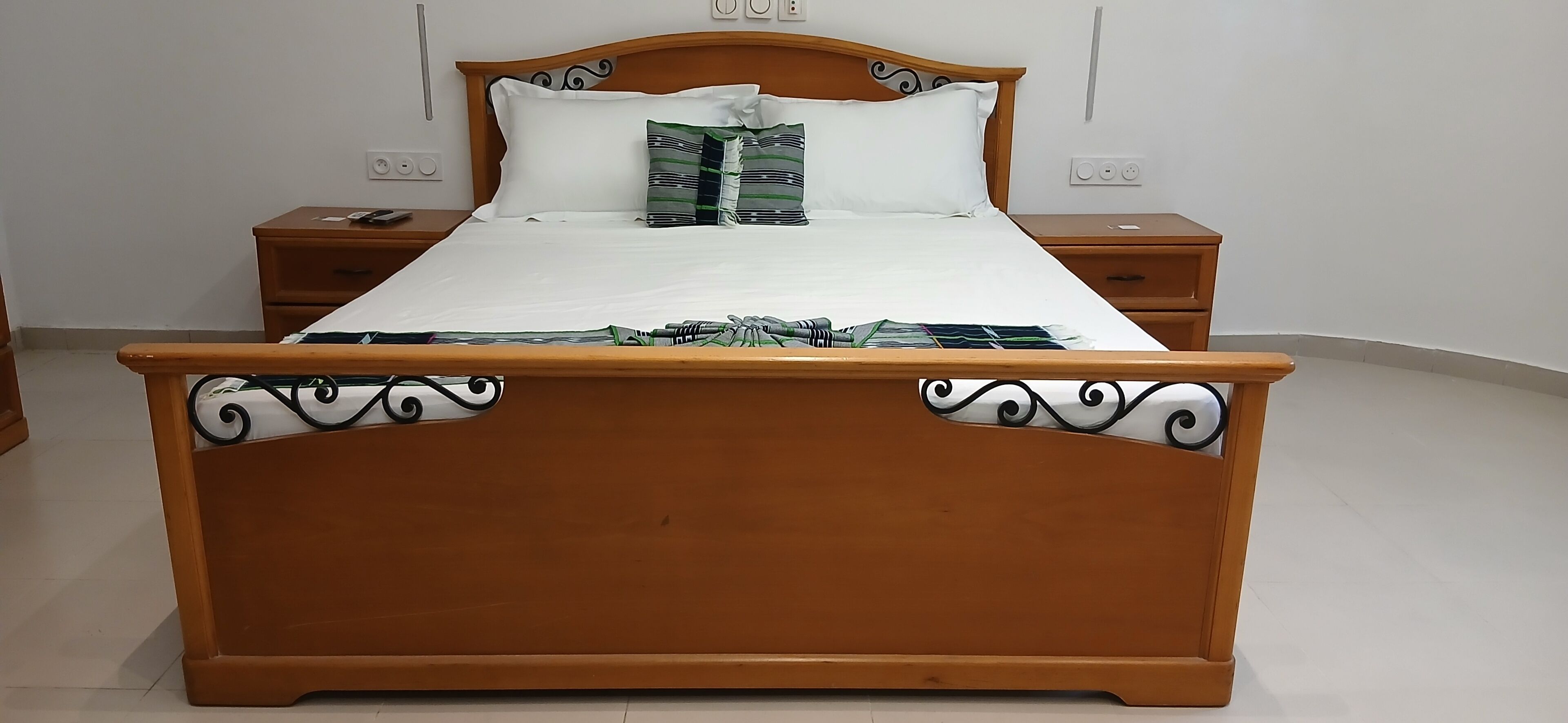 Uma cama de madeira com cabeceira, duas mesas de cabeceira e um colchão branco.