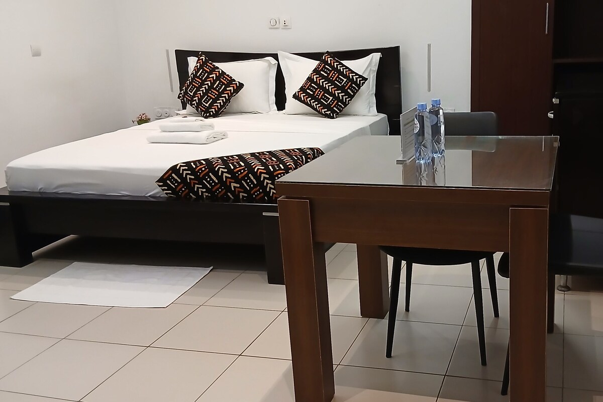 A bedroom with a bed, bedside table, chair, and a desk with a chair.
