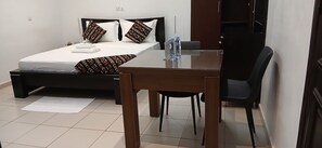 A bedroom with a bed, bedside table, chair, and a desk with a chair. - Sheyllo Suites Abidjan (Abidjan)