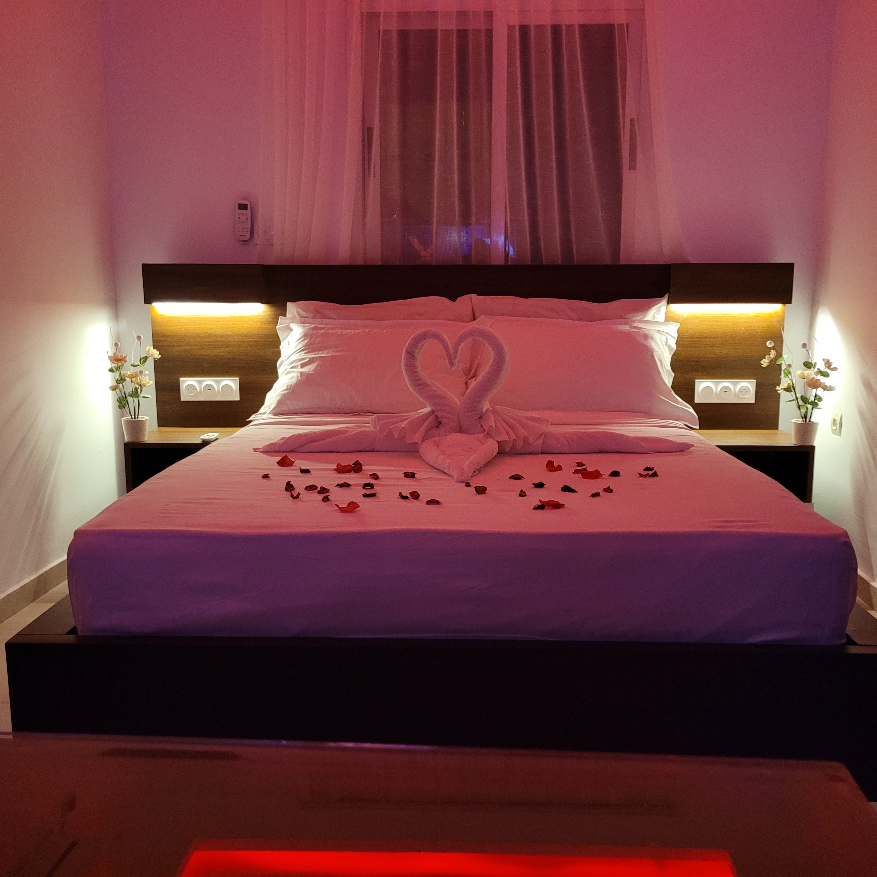 A bed with a heart-shaped towel arrangement, a bedside table with a vase, and a canopy over the bed.