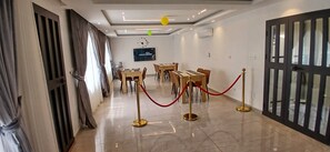 A hotel lobby with a modern design, featuring a reception desk, a seating area with tables and chairs, and a large wall-mounted television. - Sheyllo Suites Abidjan (Abidjan)