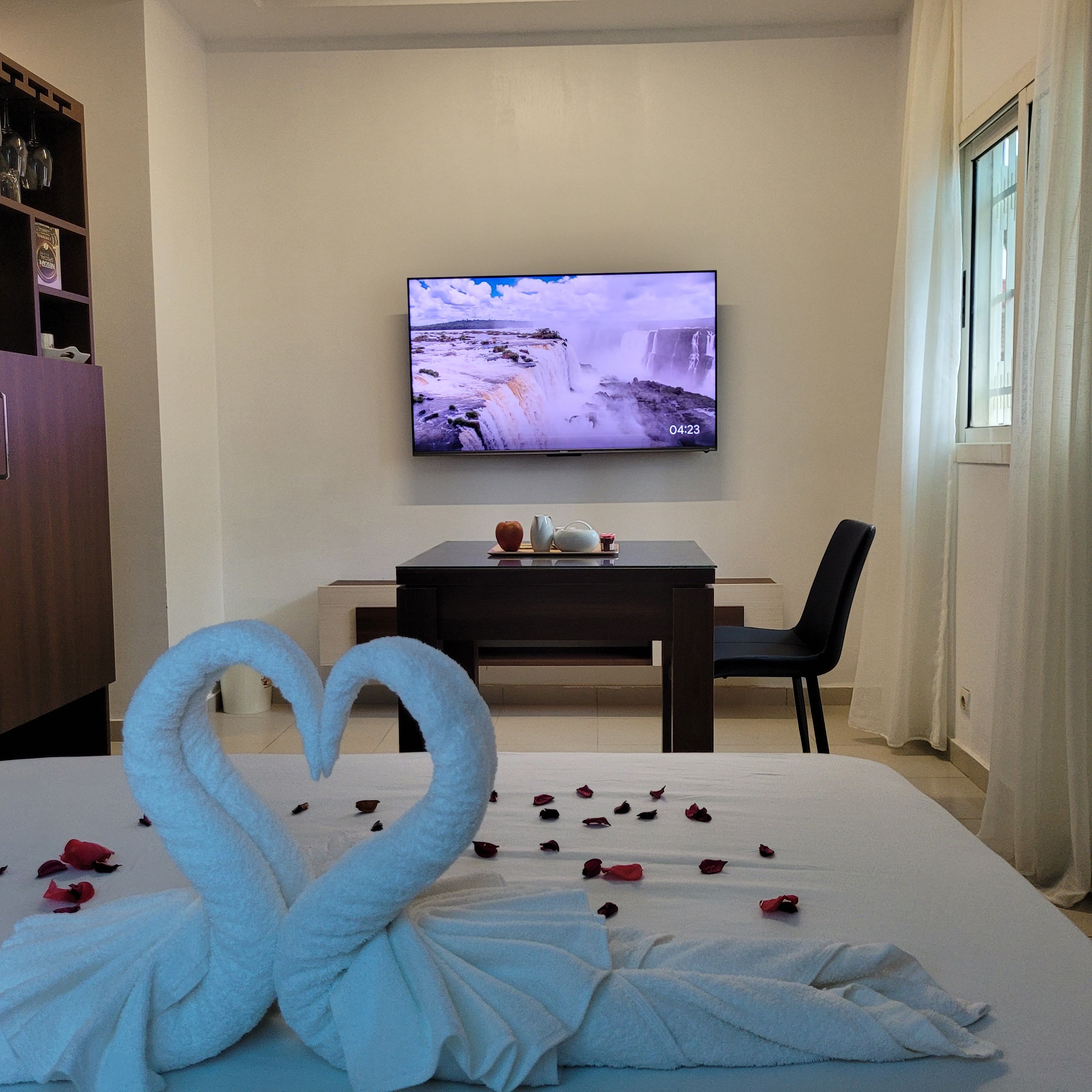 Quarto de hotel com uma cama, televisão na parede, escrivaninha e uma cadeira.