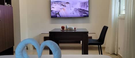 A hotel room with a bed, a TV on the wall, a desk, and a chair.