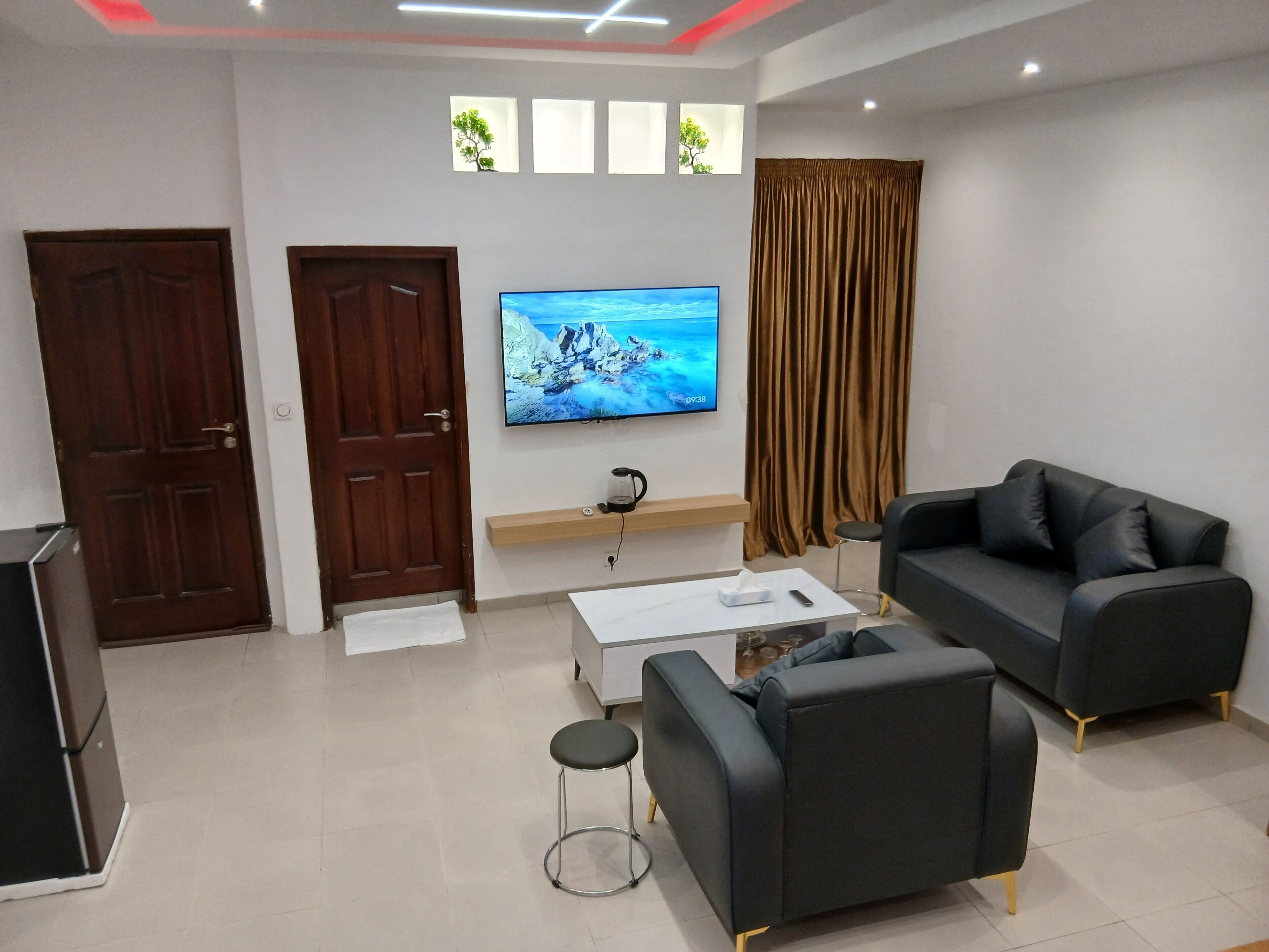 Uma sala de estar com televisão de tela plana, um sofá, uma mesa de centro e um banquinho.