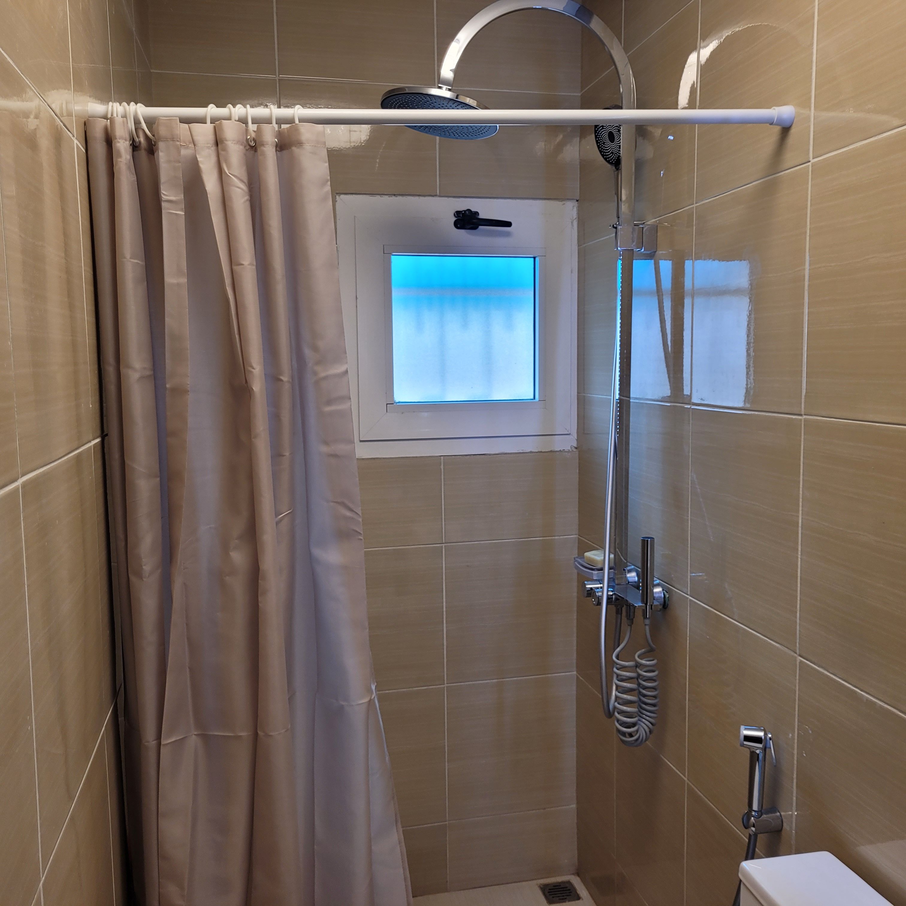 Ein Duschbereich mit Duschvorhang, Handbrause, Fenster mit Aussicht und Toilette.