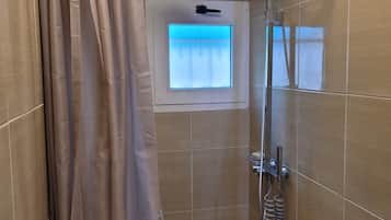 Ein Duschbereich mit Duschvorhang, Handbrause, Fenster mit Aussicht und Toilette.