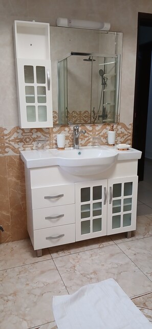 A bathroom with a white vanity, a large mirror, and a shower enclosure. - Sheyllo Suites Abidjan (Abidjan)