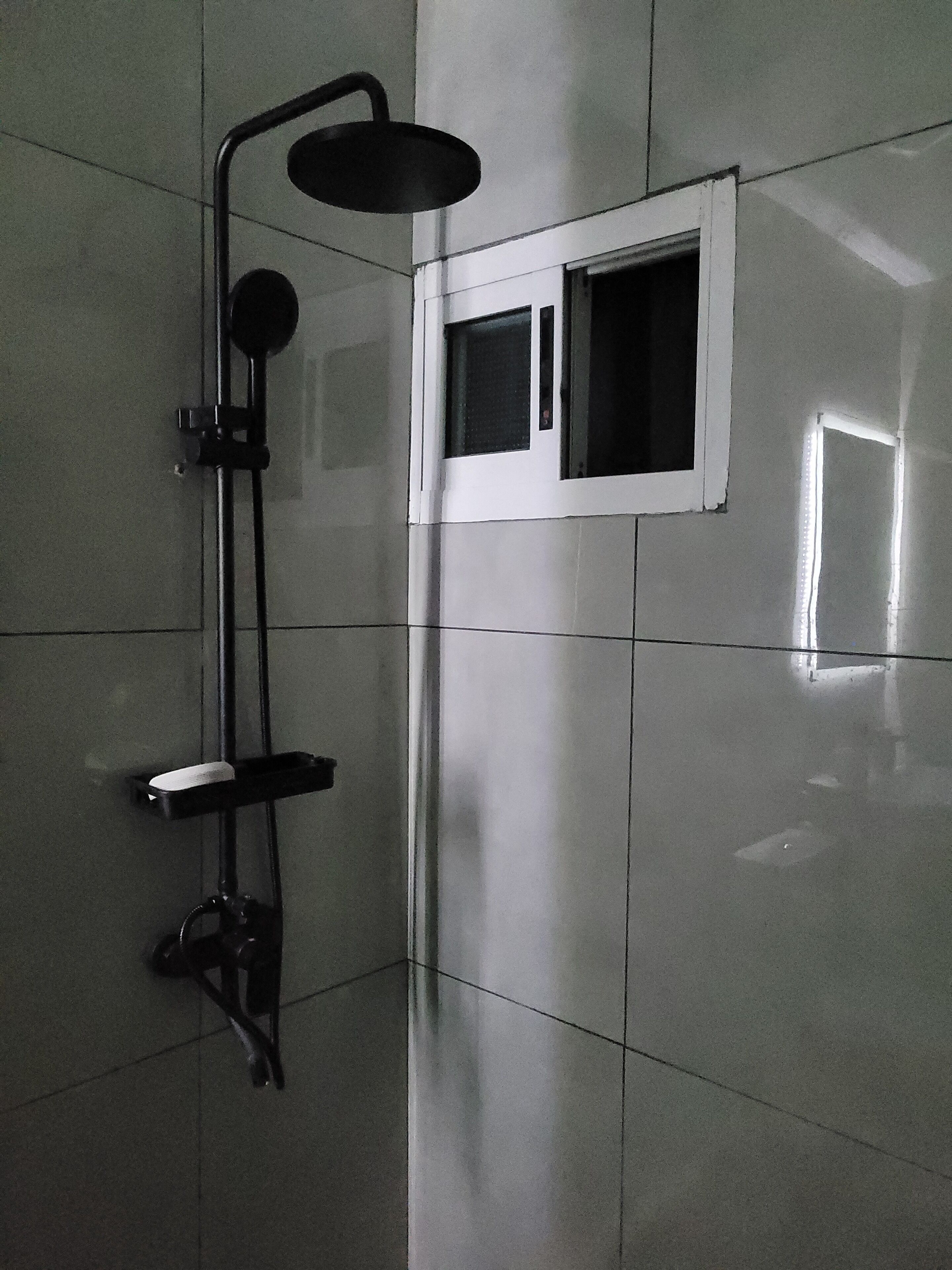 A modern bathroom with a shower, a small window, and a mirror.