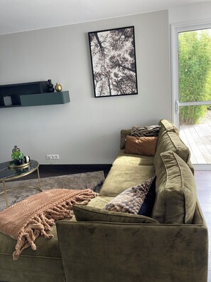 A living room with a green sofa, a black and white framed picture on the wall, and a small table with a plant. - Charming House in Névez – Spa, Sauna, Pool, and Rospico Beach Within Walking Distance (Névez)