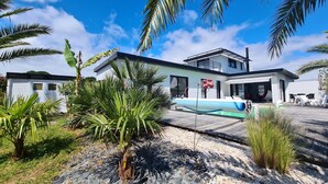 A modern house with a pool, surrounded by tropical plants and a clear sky. - Charming House in Névez – Spa, Sauna, Pool, and Rospico Beach Within Walking Distance (Névez)
