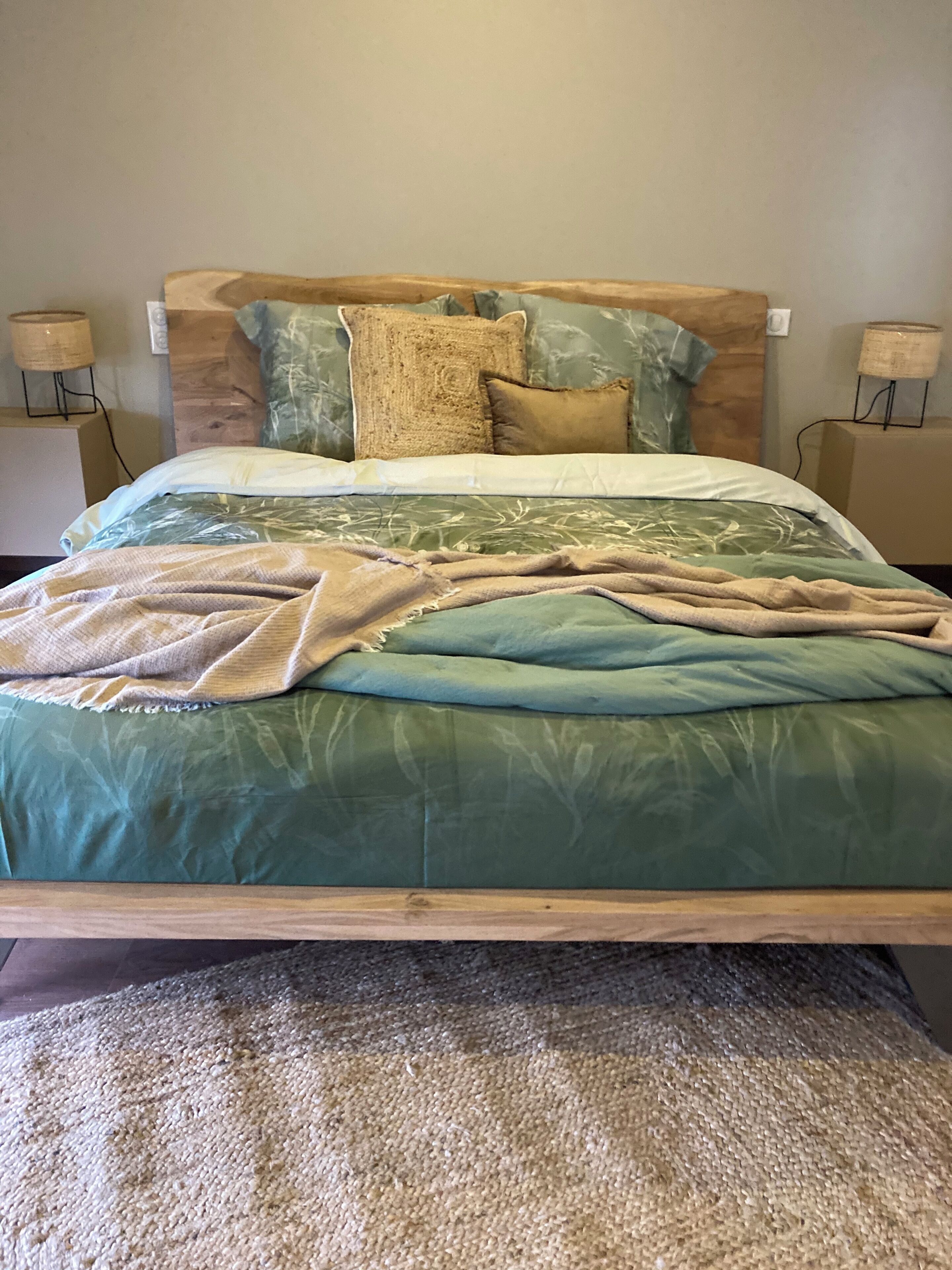 Una cama con estructura de madera, ropa de cama verde y una manta color beige.
