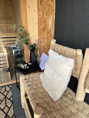 Ein Zimmer mit einem gewobenen Sofa, einem kleinen Tisch mit einer schwarzen Ablage, einer Topfpflanze und einer Holztür.