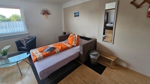 Habitación de hotel pequeña con una cama individual, un escritorio, una silla, un ventanal y un espejo.