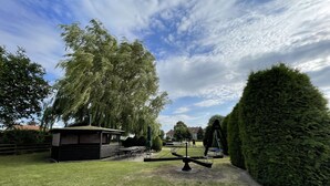 Un parque con un sube y baja, mesas de picnic y un pequeño refugio.