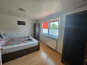 Ein Schlafzimmer mit einem Bett, einem Heizkörper, einem Fenster mit Jalousie und einer Tür.