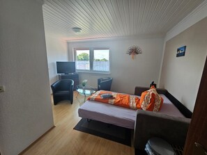 Une petite pièce comprenant un lit, un bureau, une chaise, un téléviseur et une fenêtre.