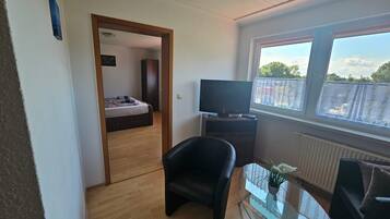Ein Zimmer mit einem Bett, einem Fernseher, einem Glastisch mit Pflanze und einem Fenster mit Aussicht.