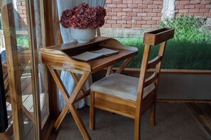 Un escritorio de madera con una silla, un florero con flores y una ventana con vistas a zonas verdes.