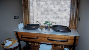 Un bagno con doppio lavabo, cassetti in legno, un piccolo ripiano con articoli da toilette e una finestra con vista.