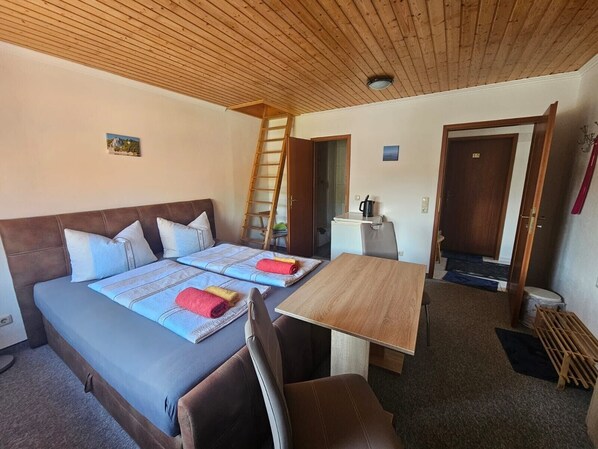 Una habitación con cama, mesa, silla, escalera y puerta.