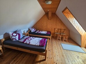 Une petite pièce avec un toit en pente, comprenant deux lits en bois, une petite table et deux chaises.