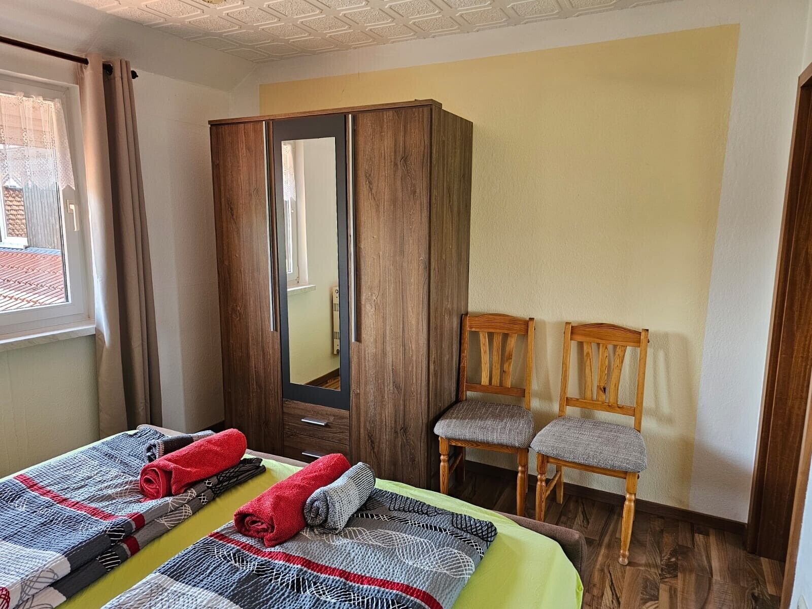 Ein Schlafzimmer mit einem Bett, zwei Stühlen, einem Kleiderschrank und einem Fenster.