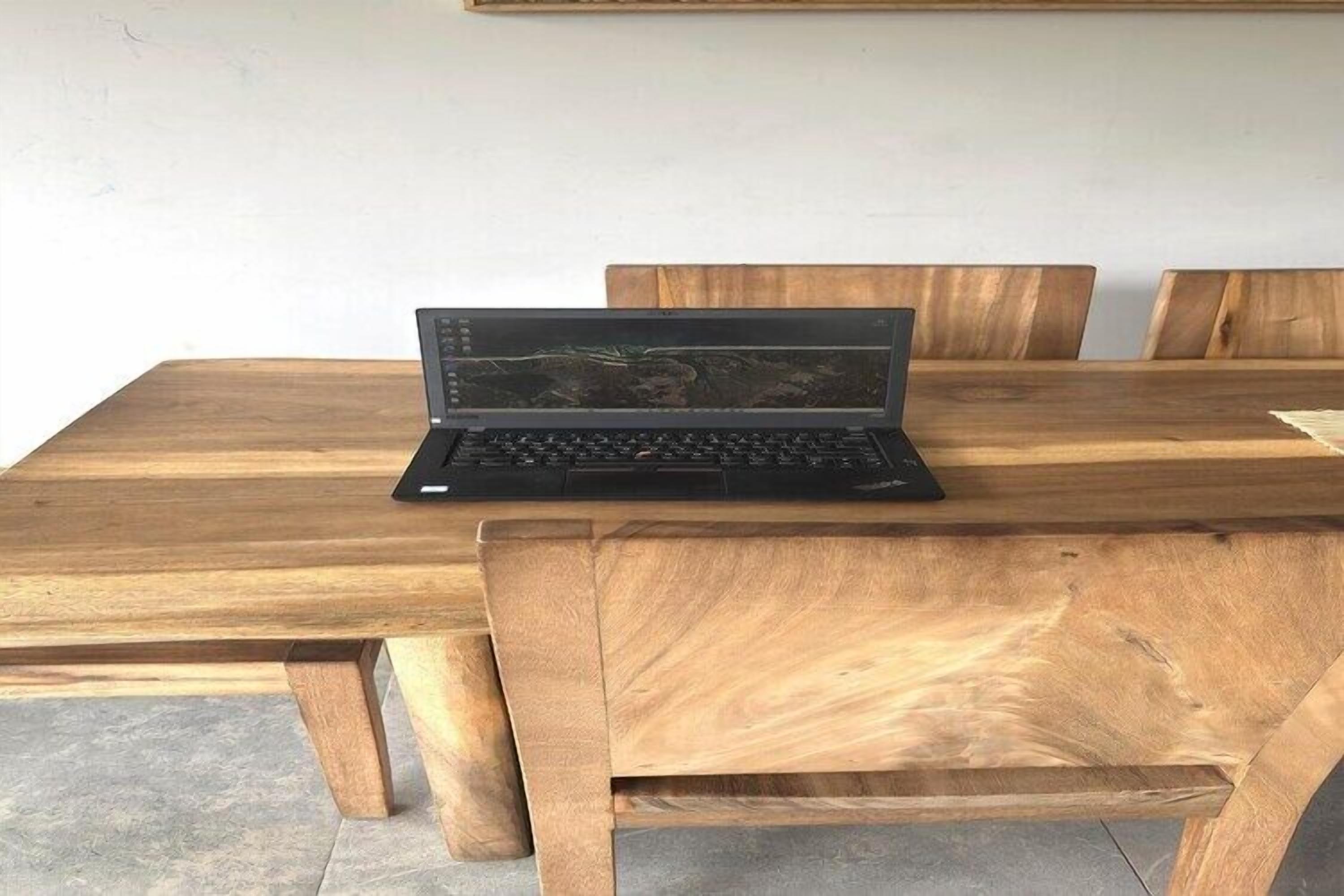 A laptop on a wooden dining table with chairs around it.