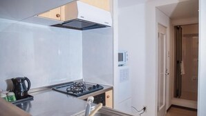 A kitchen with a gas stove, a kettle, and a microwave. - SHINKA HOTEL (Sapporo)