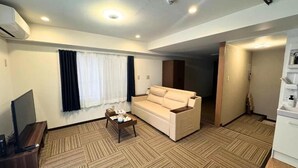 A hotel room with a sofa, a coffee table, a TV, and a kitchenette. - SHINKA HOTEL (Sapporo)