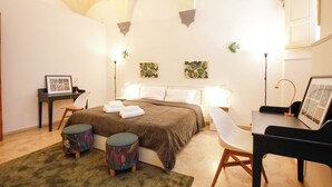 Ein Schlafzimmer mit Bett, Nachttischen, Schreibtisch, Stuhl und einem kleinen Hocker.