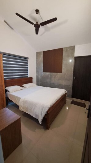 Un dormitorio con cama, cabecera de madera, ventilador de techo, armario y ventana con persianas.