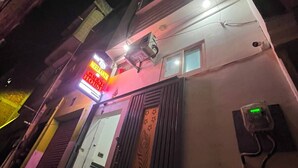 A building with a neon sign indicating a guest house, a door with a decorative panel, and a small window. - Neelkanth PG House (Varanasi)