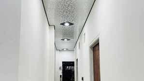 A hallway with white walls, a patterned ceiling, and a marble floor. - Neelkanth PG House (Varanasi)