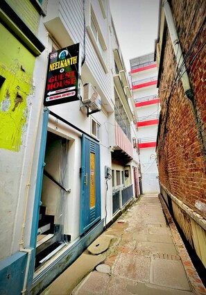 A narrow alleyway with a building on the left displaying a sign for a guest house. - Neelkanth PG House (Varanasi)