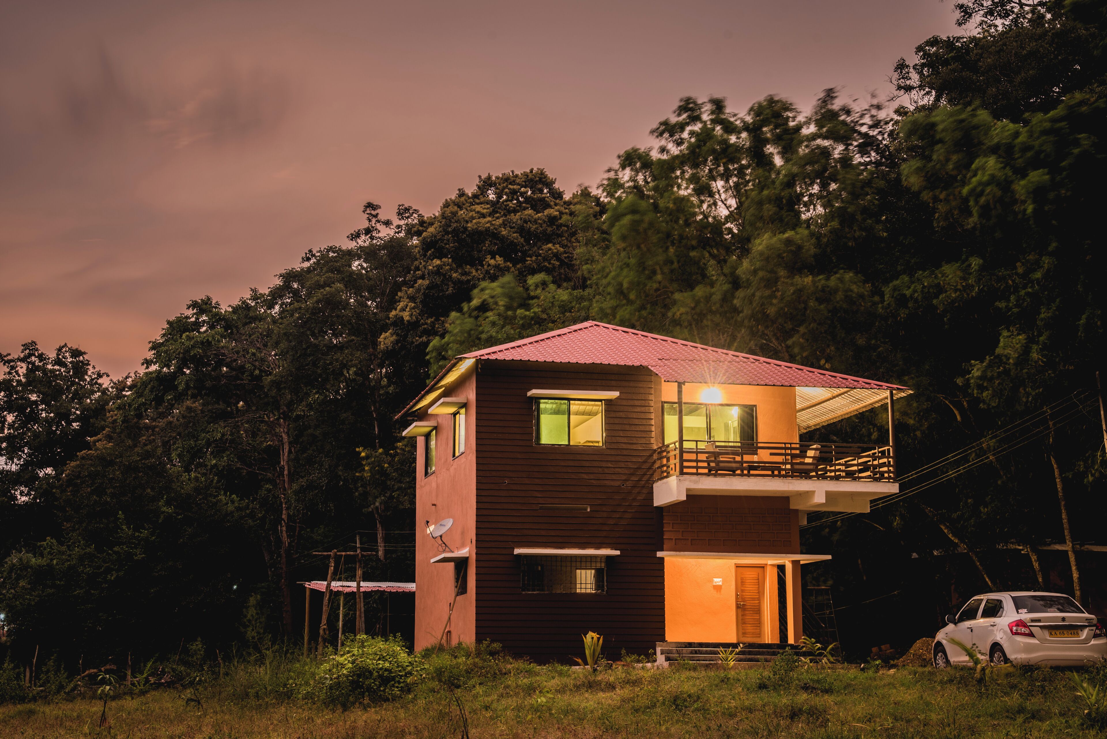 A two-story house with a balcony, surrounded by trees.